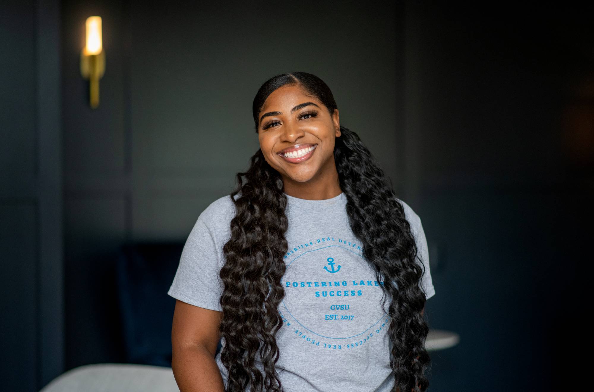 Photo of  FLS Participant Elaina  ( female,  gray t-shit blue lettering,  in a office background)